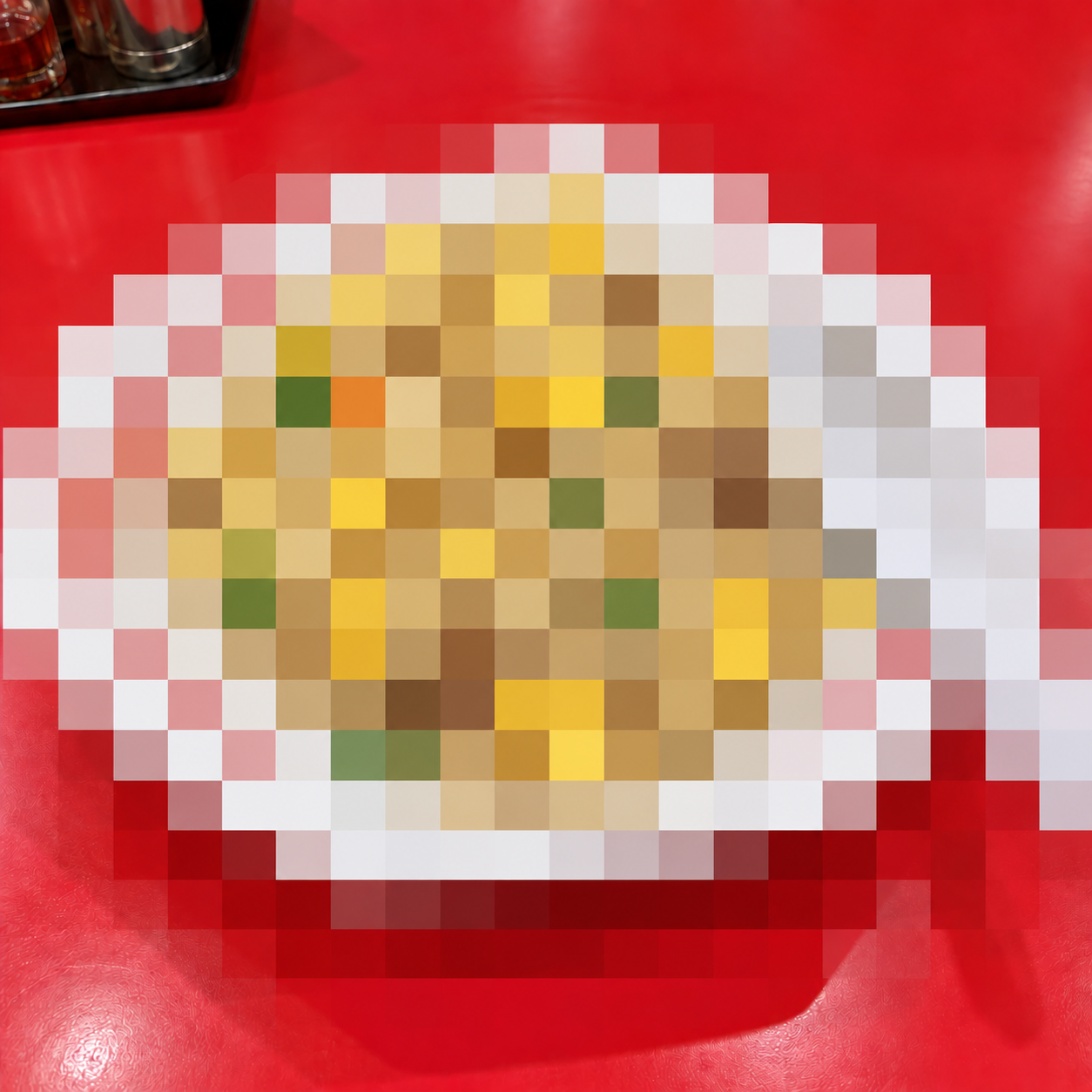 赤いテーブルの上のチャーハン。皿とレンゲにも大きなモザイクがかかった画像。